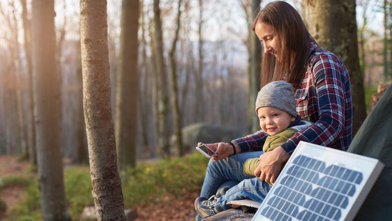 Eine Mutter mit Baby auf dem Schoß nutzt Solarstrom für ihr Handy.